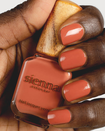 terracotta nail polish hand swatch on dark skin tone holding a sienna bottle up close