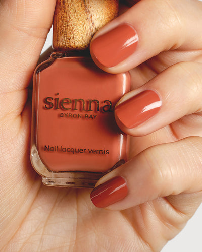 terracotta nail polish hand swatch on fair skin tone holding a sienna bottle up close
