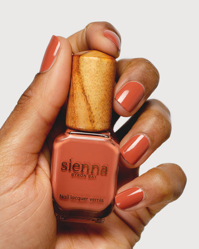 terracotta nail polish hand swatch on medium skin tone holding a sienna bottle