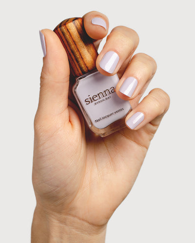 Pastel purple-grey nail polish hand swatch on fair skin tone holding a sienna bottle