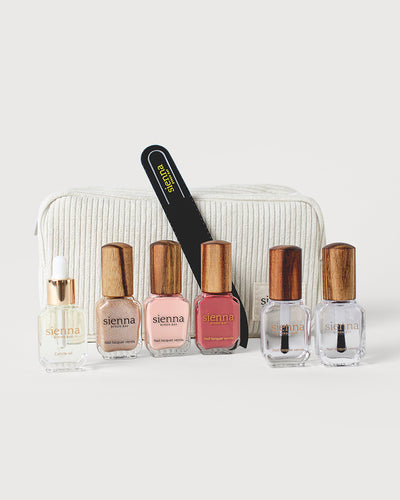 trio of white and pink nail polish with timber caps sitting to the left and a duo of clear nail polish sitting to the right with a glass nail file and cuticle oil bottle sitting in front of a white corduroy bag
