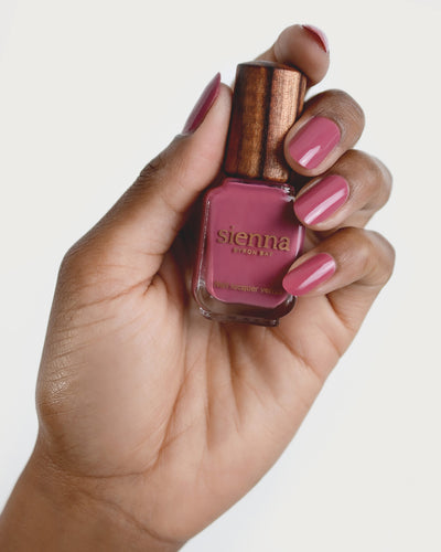 Medium tanned skin hand wearing Heartspace raspberry sorbet nail polish and holding bottle with timber lid by Sienna Byron Bay