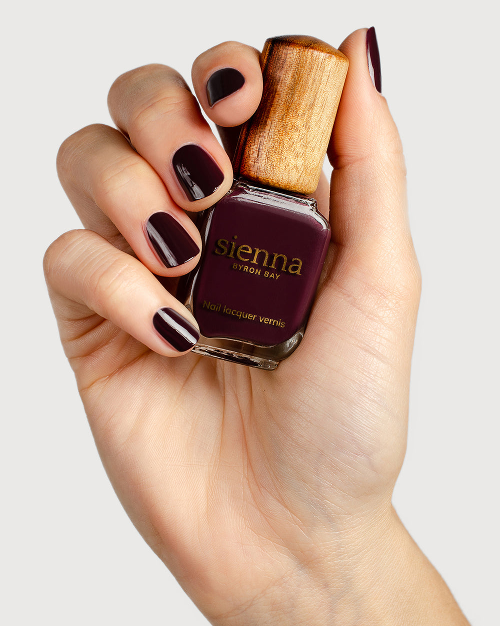 Aubergine nail polish hand swatch on fair skin tone holding sienna bottle