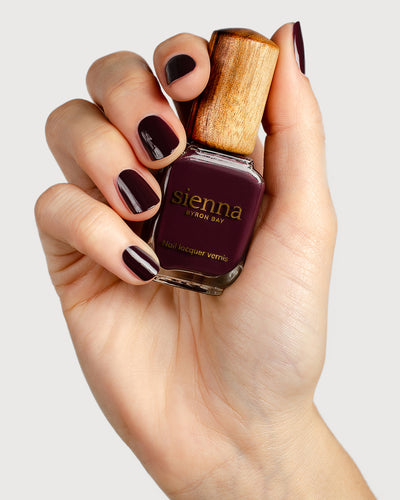 Aubergine nail polish hand swatch on fair skin tone holding sienna bottle