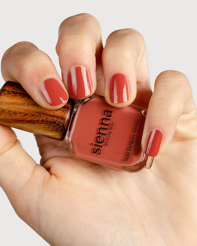 brick red nail polish hand swatch on fair skin tone holding sienna bottle