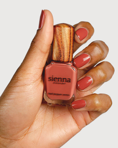 brick red nail polish hand swatch on fair skin tone holding sienna bottle