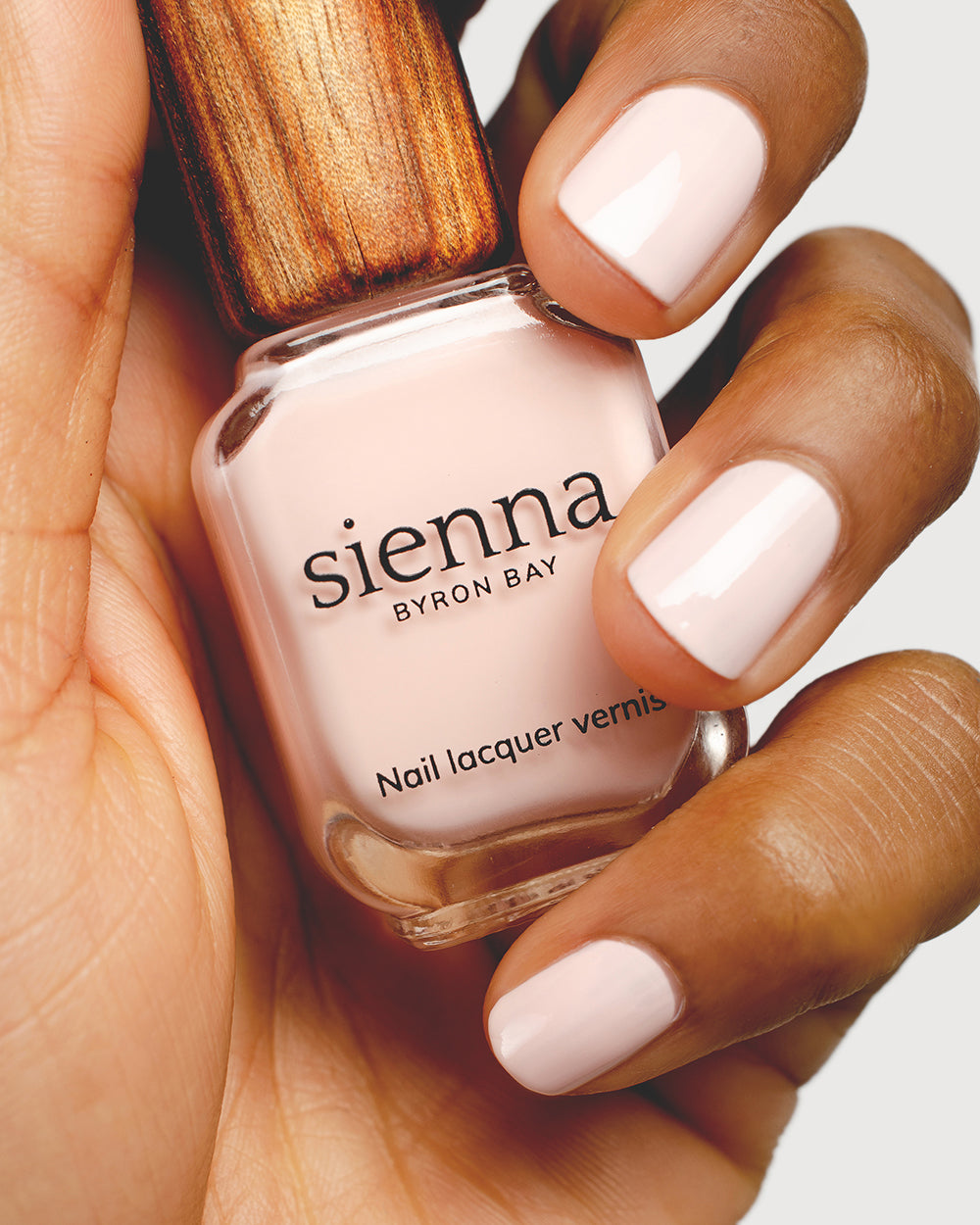 rosewater pink nail polish hand swatch on medium skin tone holding sienna bottle