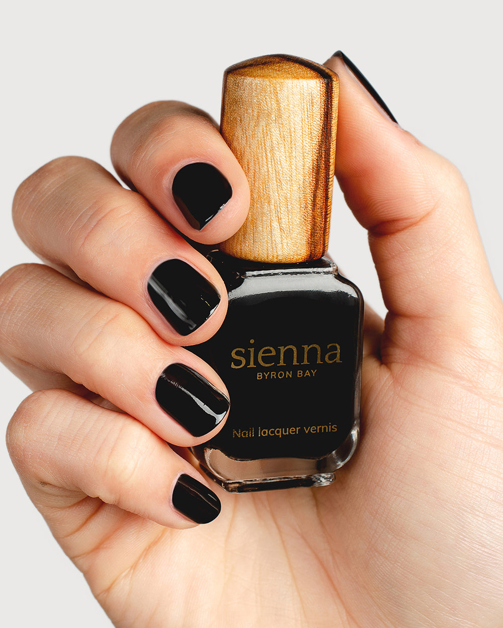 jet black nail polish hand swatch on fair skin tone holding sienna bottle