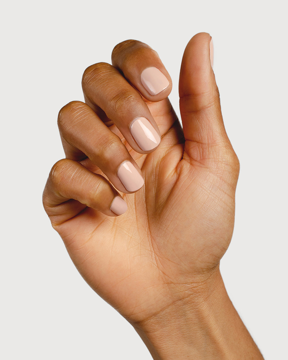 Soft neutral-pink nail polish hand swatch on medium skin tone