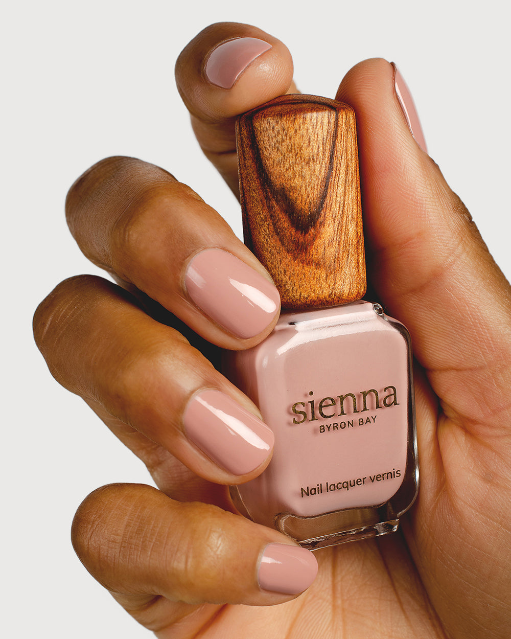 Dusty rose nail polish hand swatch on medium skin tone holding sienna bottle close-up