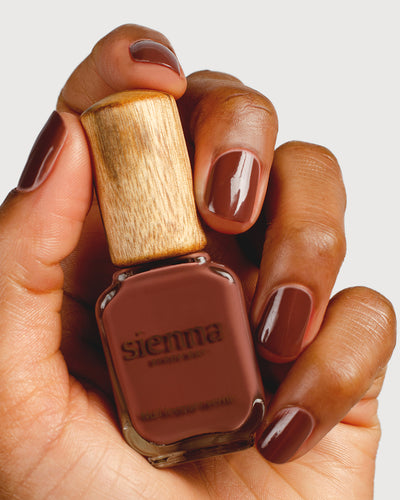 Deep burnt umber nail polish hand swatch on medium skin tone holding sienna bottle