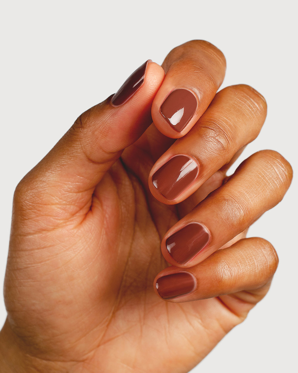 Deep burnt umber nail polish hand swatch on medium skin tone close-up
