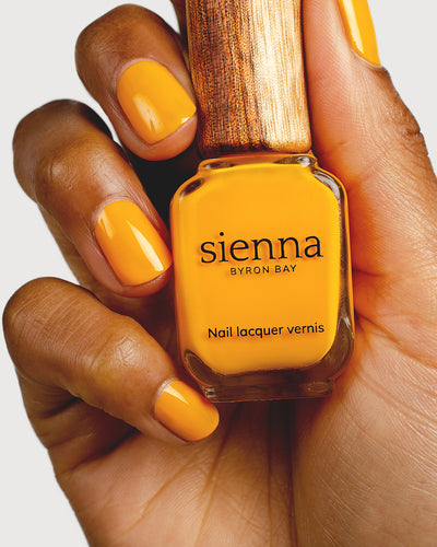 Sunflower yellow nail polish hand swatch on medium skin tone holding sienna bottle close-up