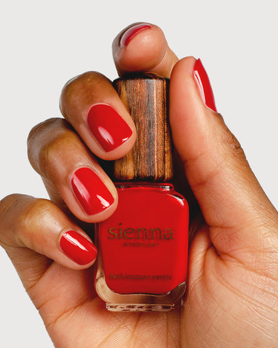 Classic red nail polish hand swatch on medium skin tone holding sienna bottle close-up
